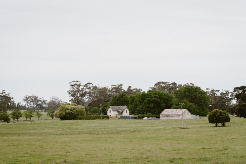 distant old English style farm house on a field with a shed - Australian Stock Image