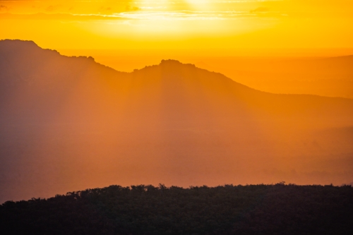 Distant view of a dramatic golden sunset over mountains with rayls of light - Australian Stock Image