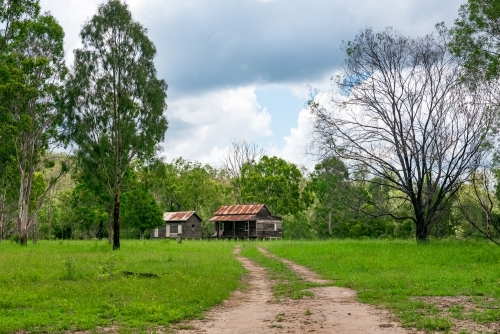 Disused wooden homestead surrounded by grazing field and dramatic stormy sky - Australian Stock Image