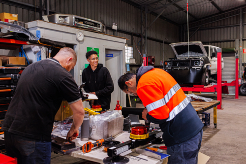 Diverse Australian workmates working together in mechanics shed fitting out new vehicles - Australian Stock Image
