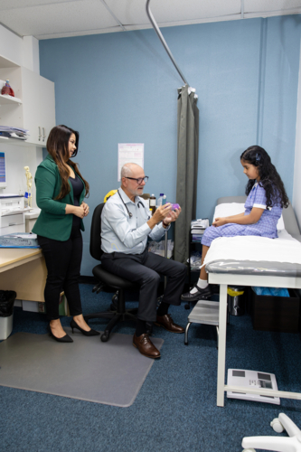 Doctor giving a girl an asthma puffer tube in office with mum - Australian Stock Image