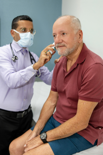 Doctor using ear thermometer on middle-aged patient - Australian Stock Image