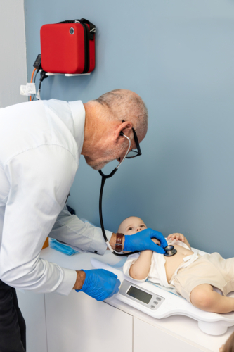 Doctor using stethoscope to listen on toddler boys tummy while lying down on a scale - Australian Stock Image