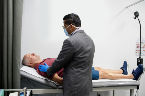 Doctor wearing blue gloves examining senior patient lying on bed - Australian Stock Image