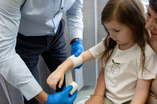 Doctor wrapping young girls arm with white bandage - Australian Stock Image