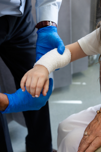 Doctor wrapping young girls arm with white bandage - Australian Stock Image
