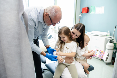 Doctor wrapping young girls arm with white bandage - Australian Stock Image