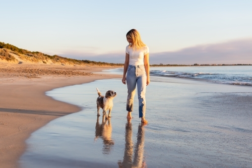 Dog and woman walking on the beach at sunset - Australian Stock Image