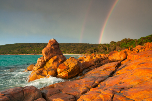 Dramatic storm lighting and a double rainbow over colourful coastal rock formations - Australian Stock Image
