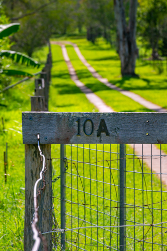 Driveway to house with vibrant green grass and wooden fence with house number in countryside - Australian Stock Image