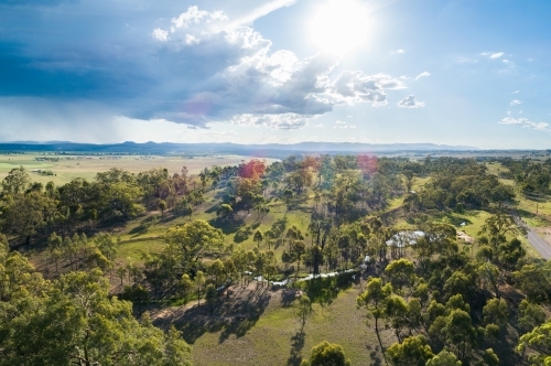 Drone photo of paddock with creek and gum trees and distant storm and rain clouds - Australian Stock Image