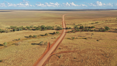 Drone shot of a dirt road going through creek and plain - Australian Stock Image