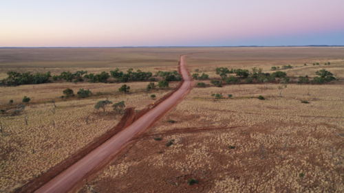 Drone shot of a dirt road going through creek and plain - Australian Stock Image