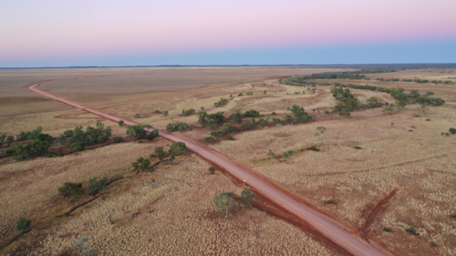 Drone shot of a dirt road going through creek and plain - Australian Stock Image