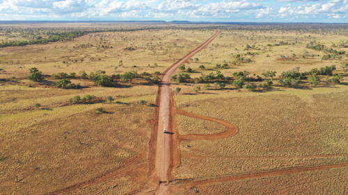 Drone shot of a vehicle driving down a dirt road - Australian Stock Image