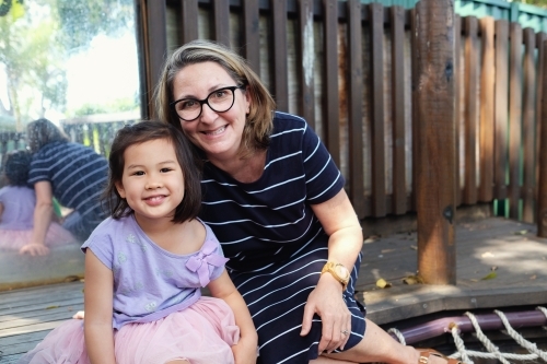 Happy multicultural teacher and child in kindergarten playground - Australian Stock Image