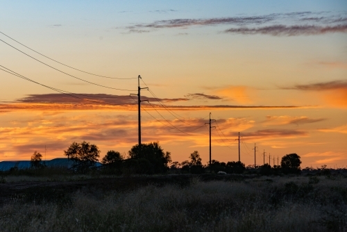 Early morning dawn colours of the sky with the power line silhouettes lead into the distance - Australian Stock Image