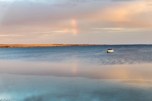 early morning light over calm bay with moored boat - Australian Stock Image
