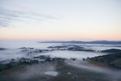Early morning mist and low-lying clouds settled in the valleys between rolling-hills. - Australian Stock Image