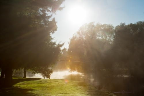 Early winter morning fog laying over river with bridge and trees - Australian Stock Image
