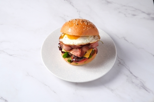 Egg and bacon burger on plate on marble table - Australian Stock Image
