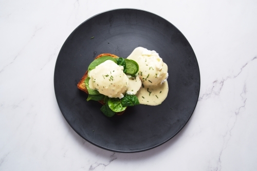 Eggs Florentine drizzled with creamy Hollandaise sauce and served on a black plate. - Australian Stock Image
