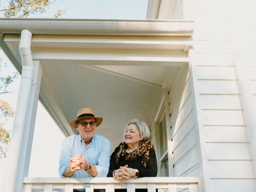 Elderly couple leaning against the wooden rails on the porch - Australian Stock Image