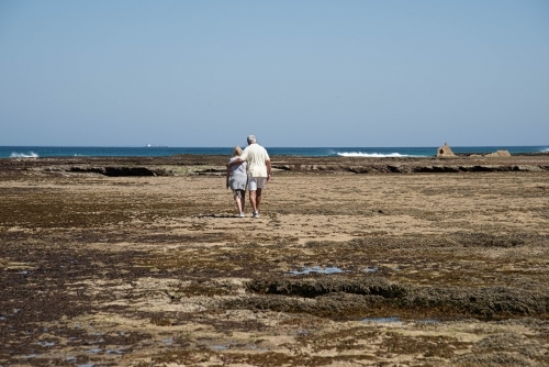 Elderly couple walking on the rocks at low tide at the beach together