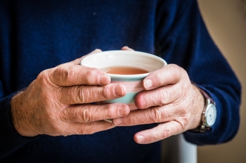 Elderly hands holding a warm cup of tea - Australian Stock Image