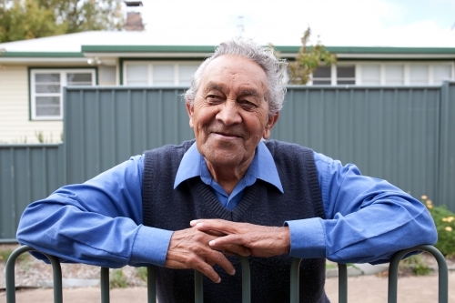 Elderly indigenous man smiling for camera while leaning on fence