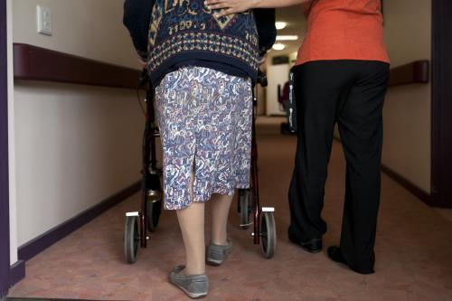 Elderly lady walking down corridor with help from nurse