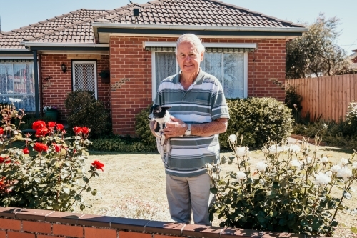 Elderly man and his little dog stand at the fence in front of his house.