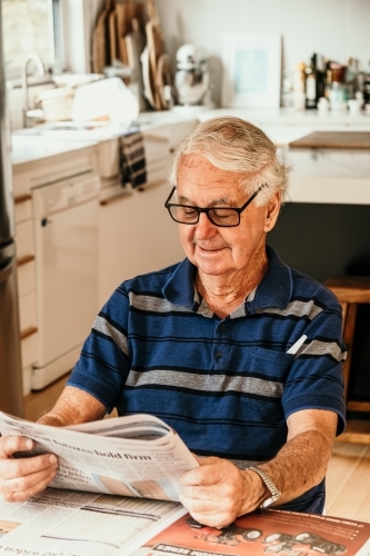 Elderly man reading newspaper in the kitchen.