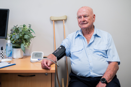 Elderly man seated near the desk with blood pressure cuff around his arm - Australian Stock Image