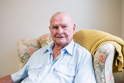Elderly man sitting comfortably on a patterned armchair indoors - Australian Stock Image