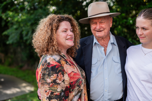 Elderly man with his daughter and granddaughter standing outdoors during family visit - Australian Stock Image