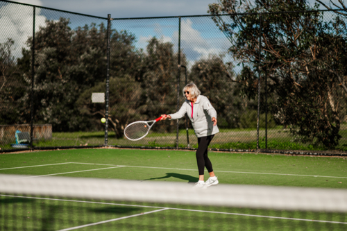 Elderly woman enjoying a tennis match on a green court outdoors - Australian Stock Image