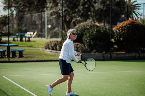 Elderly woman enjoys a game of tennis on a sunny green outdoor court - Australian Stock Image