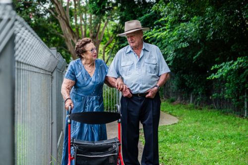Elderly woman in blue patterned dress walking with an elderly man outdoors - Australian Stock Image