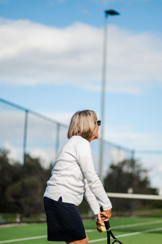 Elderly woman in sportswear prepares to hit a tennis ball on an outdoor court - Australian Stock Image