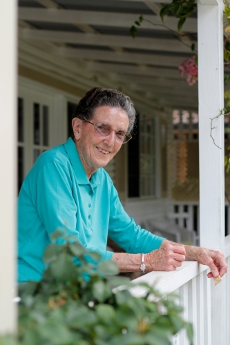 Elderly woman leaning on a verandah railing, smiling at the camera - Australian Stock Image
