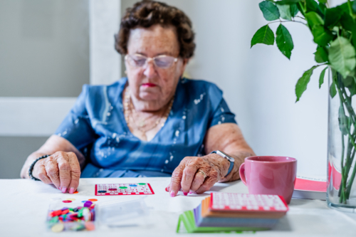 Elderly woman playing bingo cards on the table - Australian Stock Image