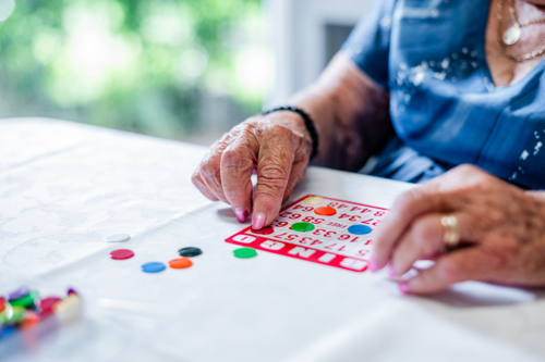 Elderly woman playing bingo cards on the table - Australian Stock Image