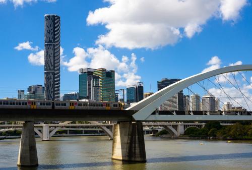 Electric train crossing railway bridge over Brisbane River with city skyline in background