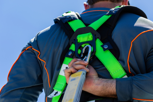 Electrician tradie man clipping rope to safety harness during construction work on roof - Australian Stock Image