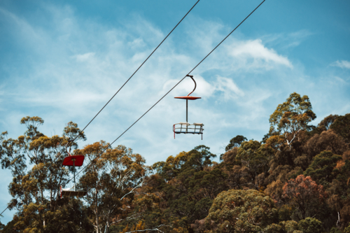 Empty chairlift gliding on steel cable above treetops. - Australian Stock Image