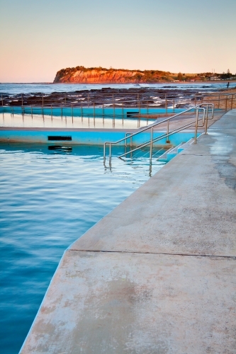 Evening light over tidal bathing pools with a bluff brightly illuminated in the distance - Australian Stock Image