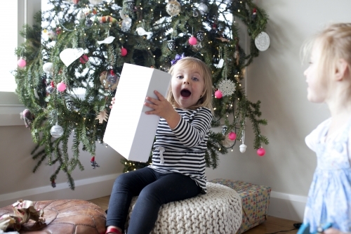 Excited young girl with present in front of Christmas tree - Australian Stock Image