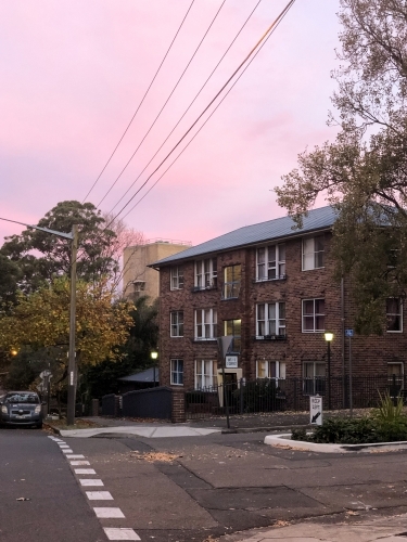facade of a building made of bricks with power lines and trees on the side with pink skies