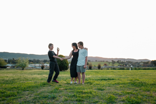 Family bonding outdoors with two boys and woman in scenic field with distant hills - Australian Stock Image
